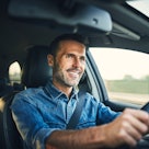 一个胡子花白、头发乌黑的男人边开车边微笑。
