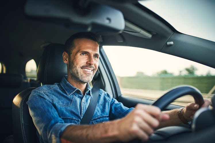 A man with a greying beard and dark hair smiling while driving his car.