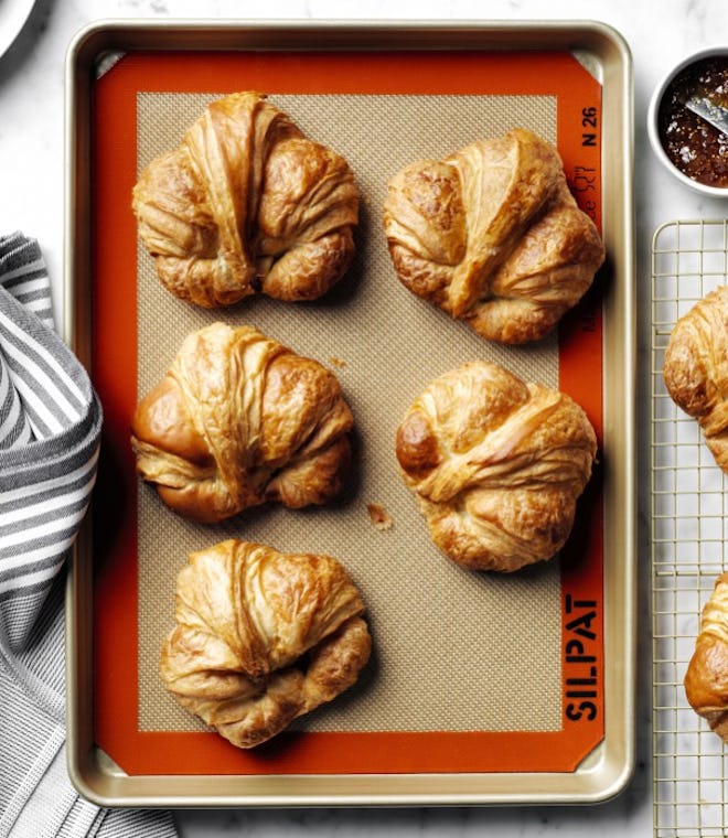 A Silpat baking mat on a sheet with fresh baked croissants on top