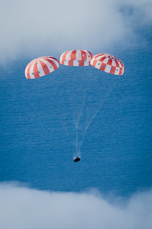 Orion spacecraft with all its parachutes deployed, with the ocean in the background and clouds above