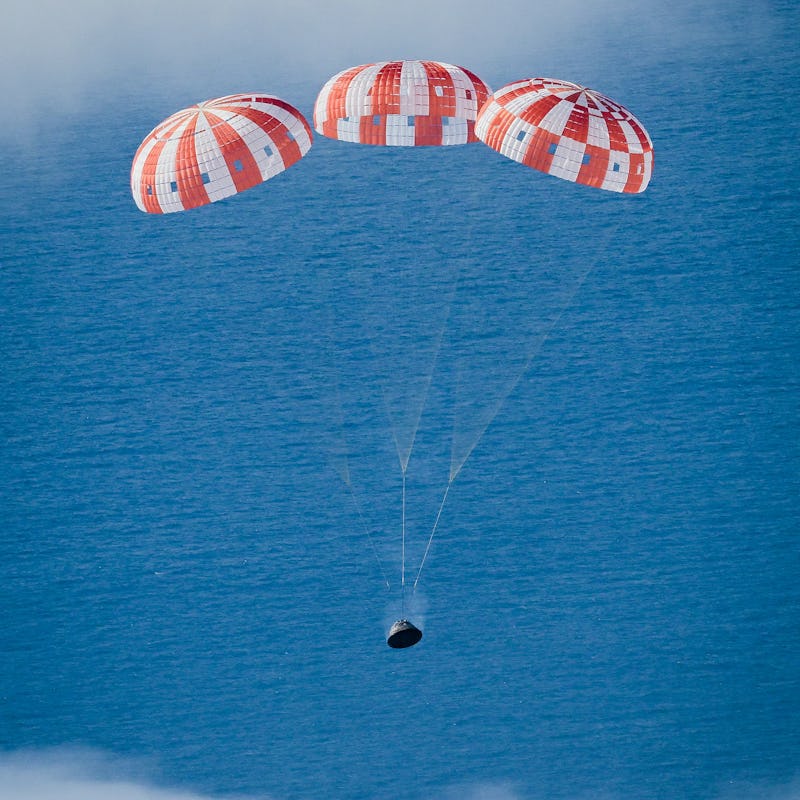 Orion spacecraft with all its parachutes deployed, with the ocean in the background and clouds above