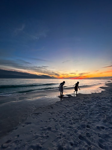 Two young girls play at the water's edge on the beach while the sun sets. Taken using iPhone photogr...