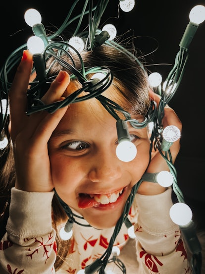 A young girl crosses her eyes and sticks out her tongue for the camera with Christmas lights framing...