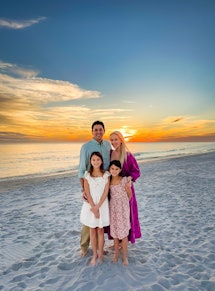 Eine Mutter, ein Vater und zwei Töchter posieren für ein Foto am Strand bei Sonnenuntergang.  Mit iPhone fotografiert...