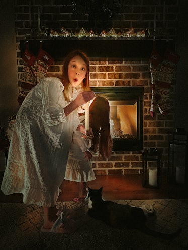 Two little girls in vintage nightgowns tiptoeing past fireplace, one holding a candlestick, in a Roc...