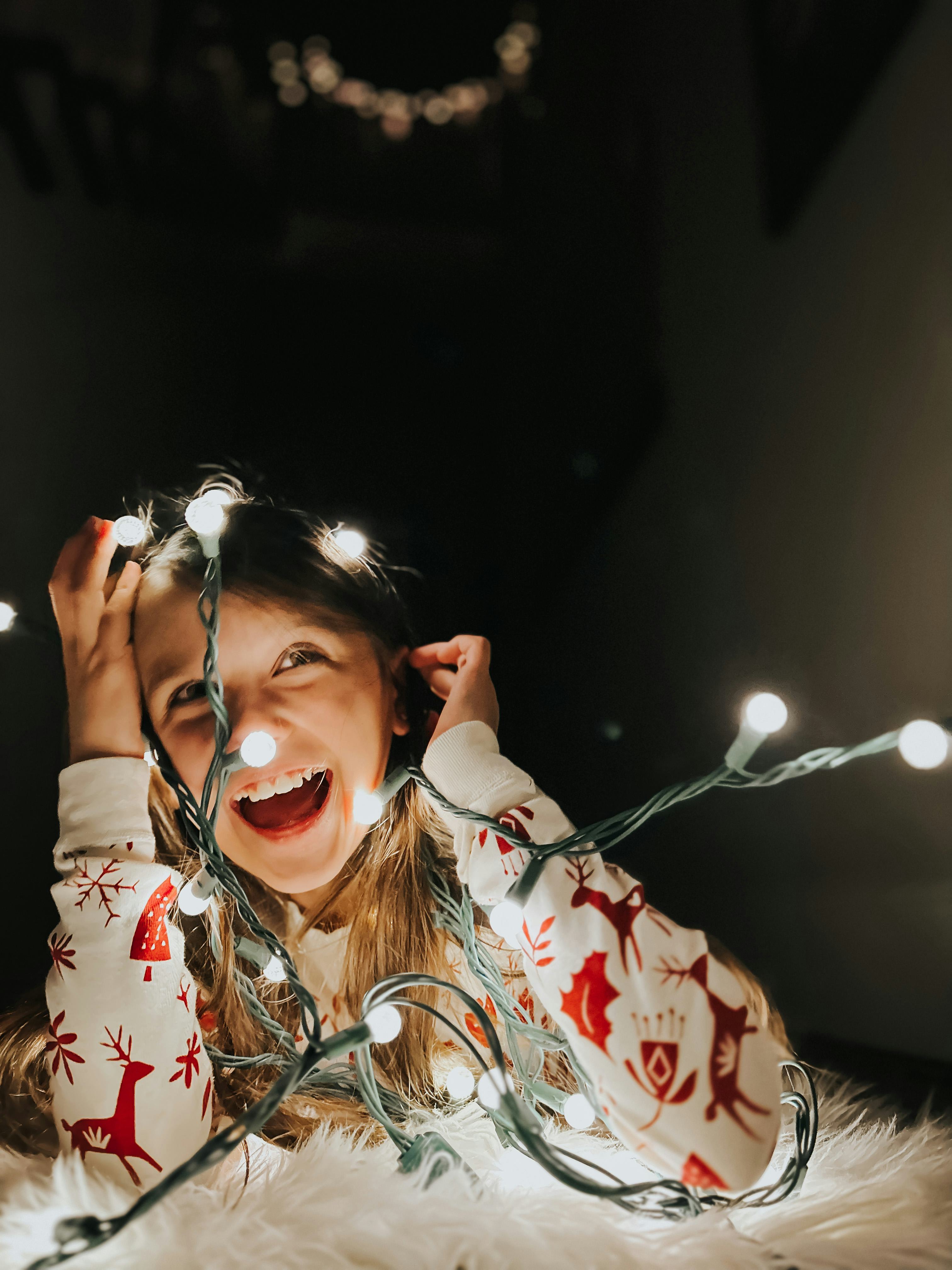 Girl in Christmas pajamas tangled in Christmas lights smiles, in tory about iPhone photography tips ...