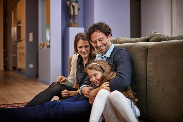 A mom and dad with their child sitting against the back of a couch.