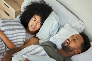 A man snoring in bed, his wife awake and upset.