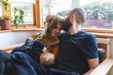 A man kissing the head of his wife as she breastfeeds their baby.