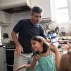 A white man dancing with his young daughter in their kitchen.