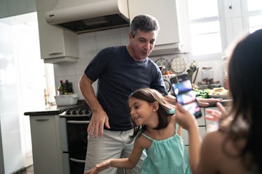 A white man dancing with his young daughter in their kitchen.