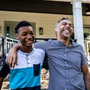 A dad has his arm around his son's shoulder while they laugh outside their home.