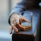 近距离的一杯威士忌休息在一个男人的皮椅的手臂末端。