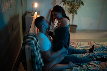 A woman sits on a man's lap seductively in bed.