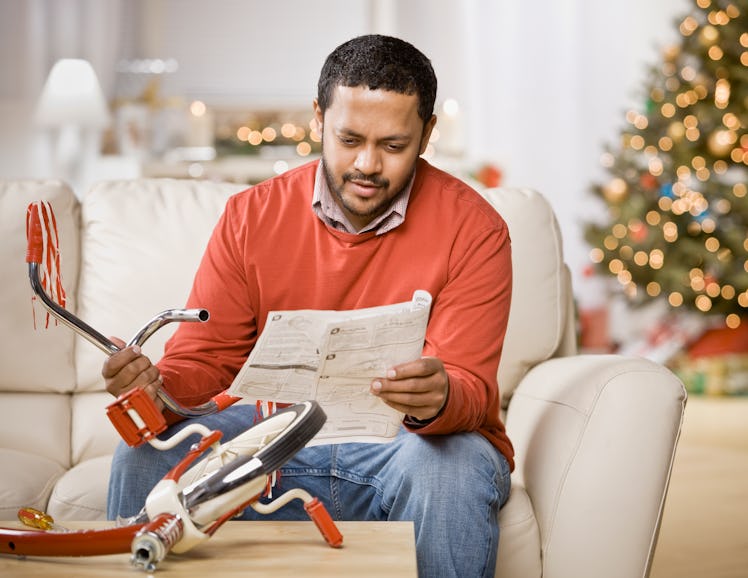 A stressed dad puts together a tricycle in front of a Christmas tree.
