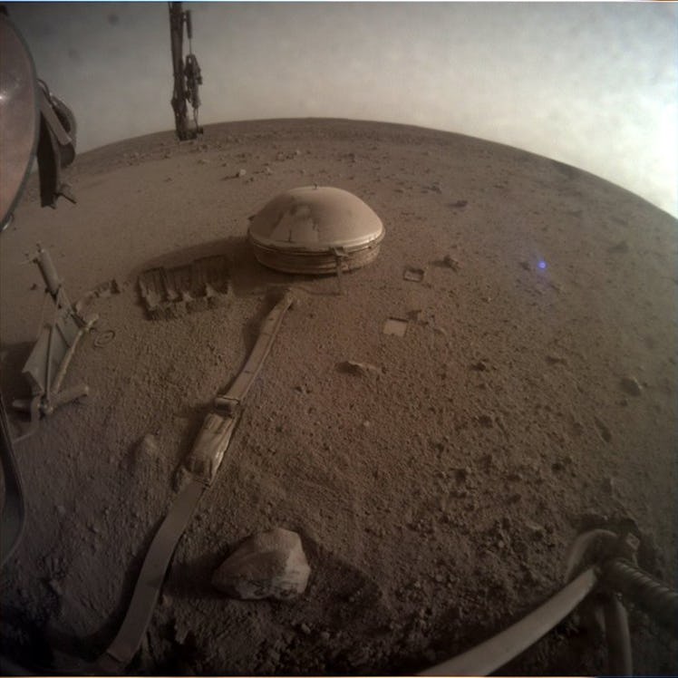 Color photo of science instruments and a lander's robotic arm on a brown, dusty Martian surface bene...