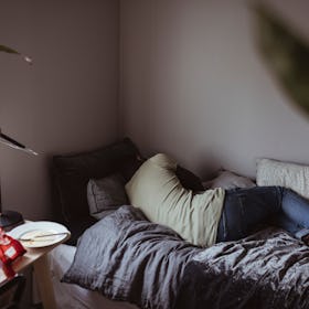 A depressed man sleeps in a small bed, facing away.