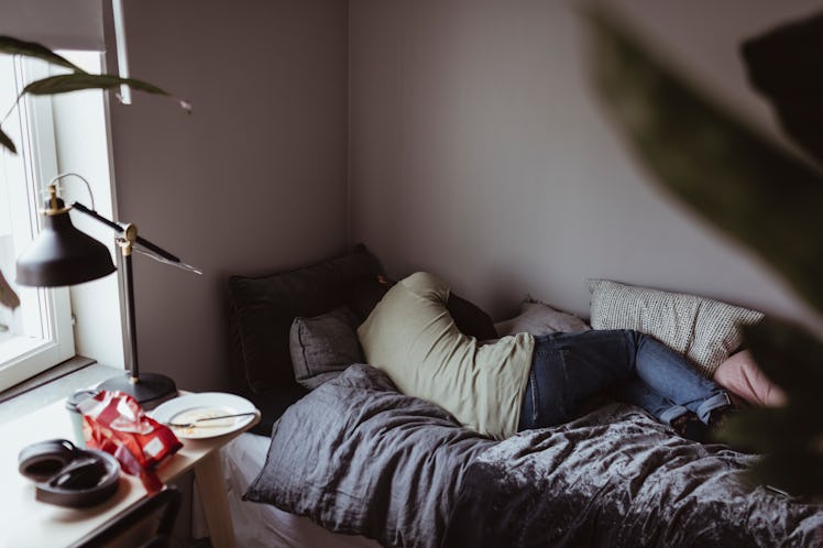 A depressed man sleeps in a small bed, facing away.
