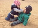 一个蹒跚学步的孩子在沙滩上推了另一个孩子的脸。