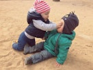 一个蹒跚学步的孩子在沙滩上推了另一个孩子的脸。