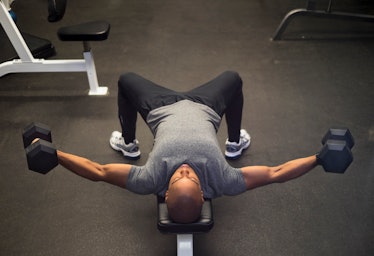 A man on a workout bench with arms straight out to the sides with dumbbells in his hands.