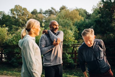 Three runners standing outdoors, stretching.