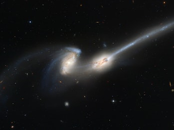 Color photo of two colliding galaxies with long glowing tails.