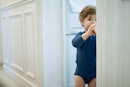 A toddler standing in a doorway while drinking milk from a bottle.