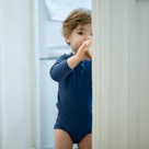 一个蹒跚学步的孩子站在门口，从瓶子里喝牛奶。