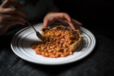 Close up of a person eating baked beans and quiche.