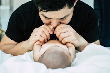 A father sniffs his baby, who is lying down.