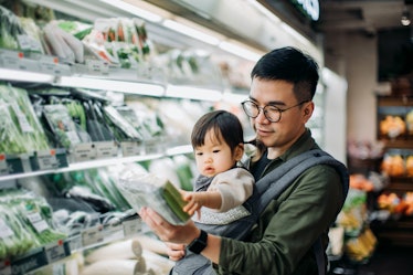 A dad and his child shopping for vegetables in a grocery store.