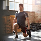 A man doing lunges with kettlebells in a gym