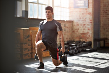 A man doing lunges with kettlebells in a gym.