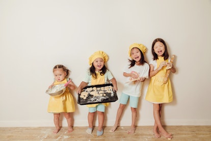 four little asian girls in a yellow apron and a chef's cap look at the camera and show the cookies t...