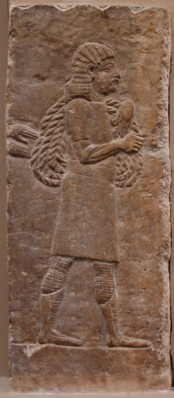 A relief detail showing a man carrying ropes with the hand of someone carrying a log and traces of w...