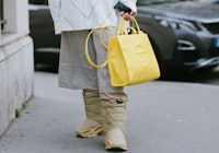 A guest poses wearing a Yellow Prada bucket hat, Yeezy boots and a Telfar bag 