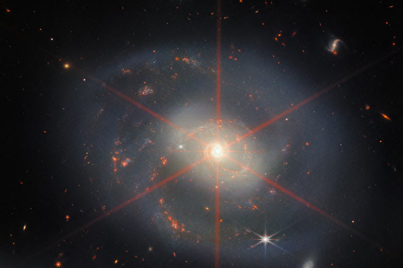 A face-on galaxy, with gray spiral arms, sprinkled with bright red patches of star formation. Its ce...
