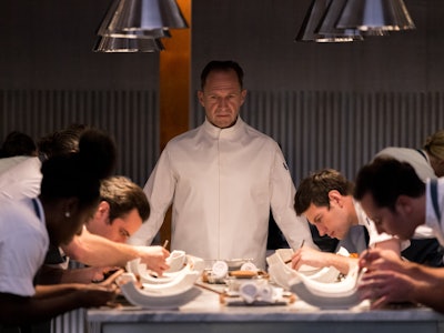 Chef Slowik (Ralph Fiennes) stands in front of a team of chefs in The Menu
