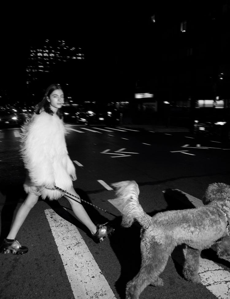 Model Loli Bahia walking a dog and wearing white fur coat.