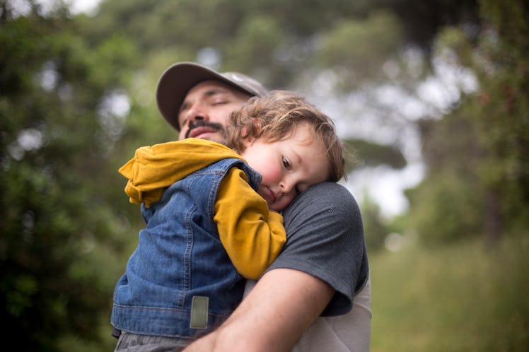 A dad holding his embarrassed toddler in a hug.