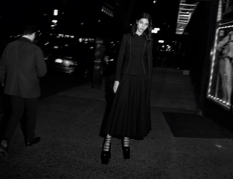 Model Loli Bahia standing outdoors wearing a black skirt suit.