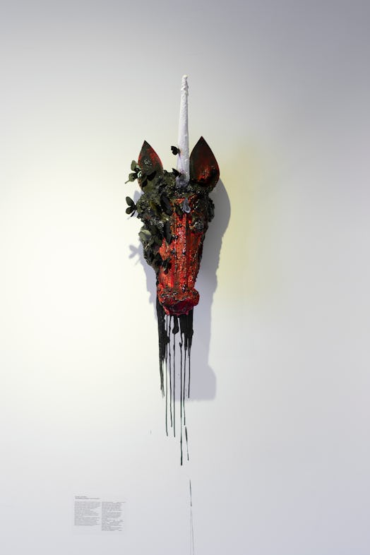 an art piece of a red and black unicorn head mounted on a white wall.