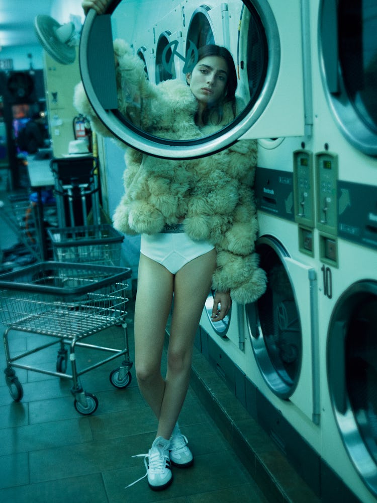 Model Loli Bahia standing in a laundry mat wearing white underwear and a fur coat.