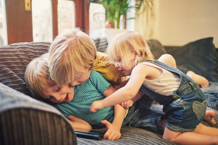 Two brothers and a sister on a couch, playing with a tablet.
