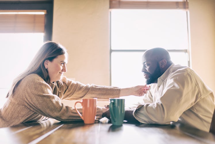 A woman reaching out across a table and touching her husband's face.