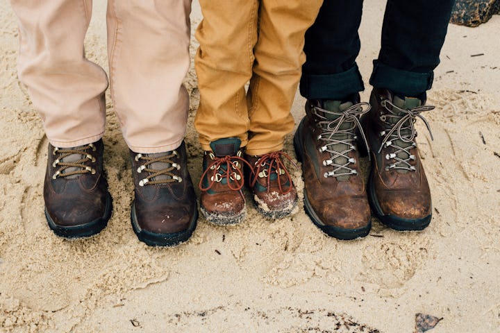 Close up of three men's boots as they stand in sand.