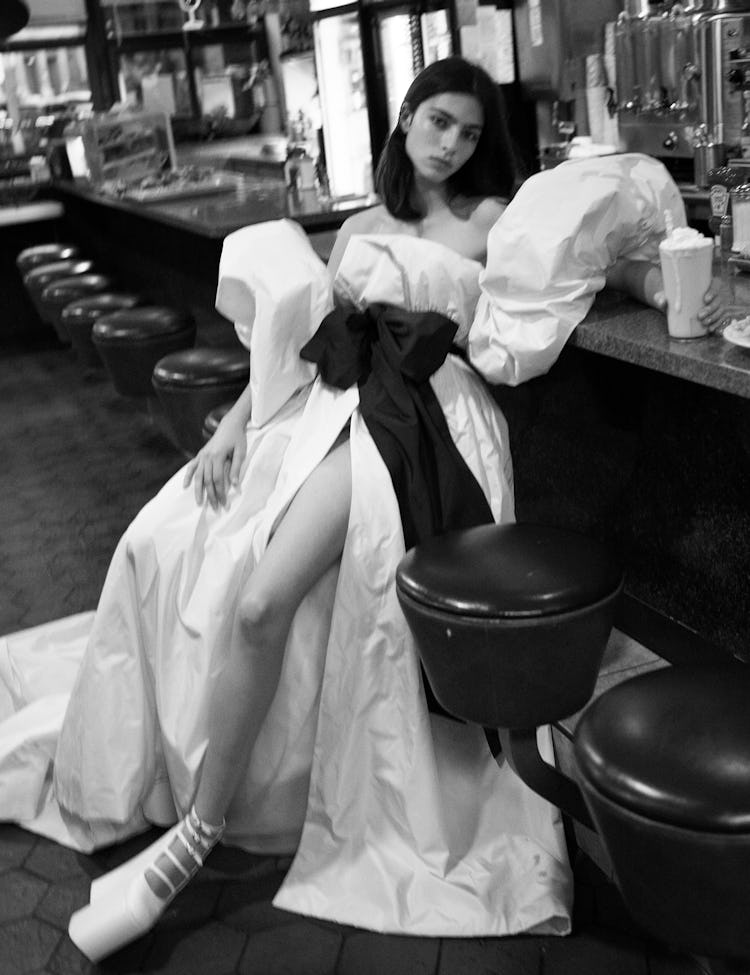 Model wearing a white gown and white platform shoes.