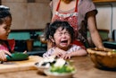 当妈妈准备食物时，一个蹒跚学步的孩子在餐桌上发脾气。