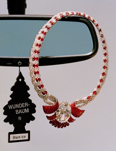 a Van Cleef & Arpels necklace dangling from a rear view mirror next to an air freshener